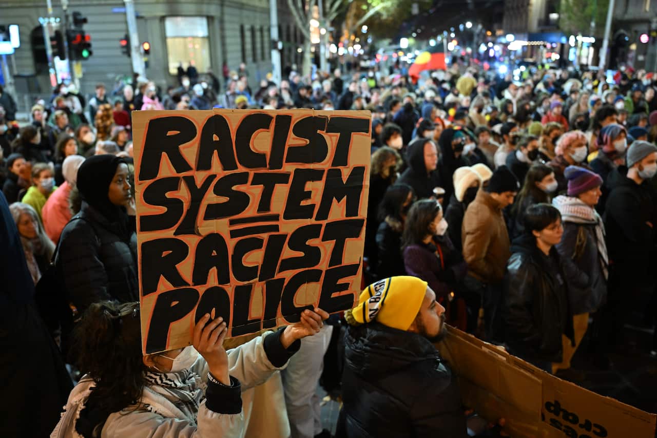 A protester holds up a sign at a rally, the people behind the sign are blurred
