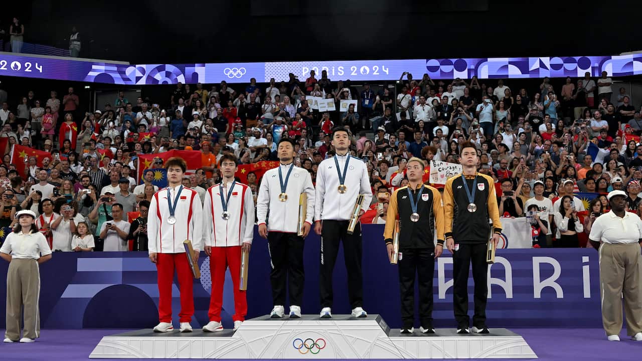 Two Taiwan athletes stands on the top of an olympic dias with medals around their neck, the Chinese team on second place and another team on third.