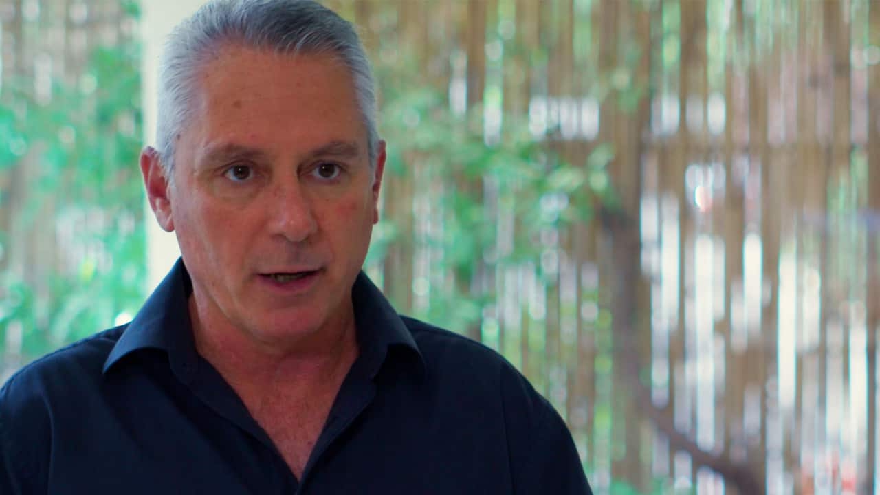 A man with grey hair and wearing a blue shirt speaking 