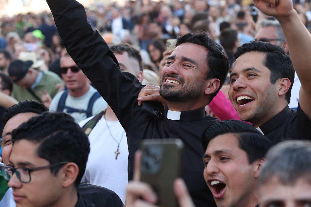 Two catholic priests cheer with their arms around each other in a jubilant crowd.