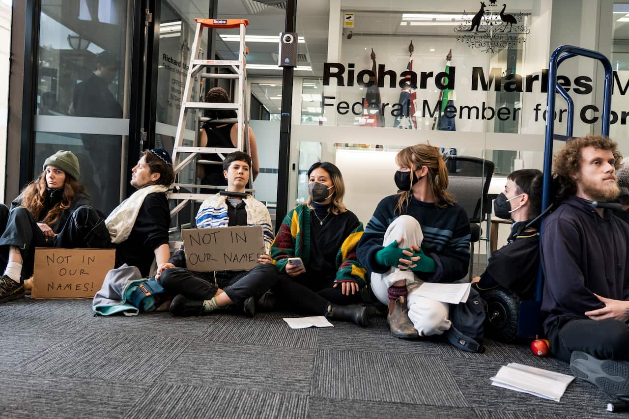 Protesters seated on the ground. Some have their necks chained to objects.