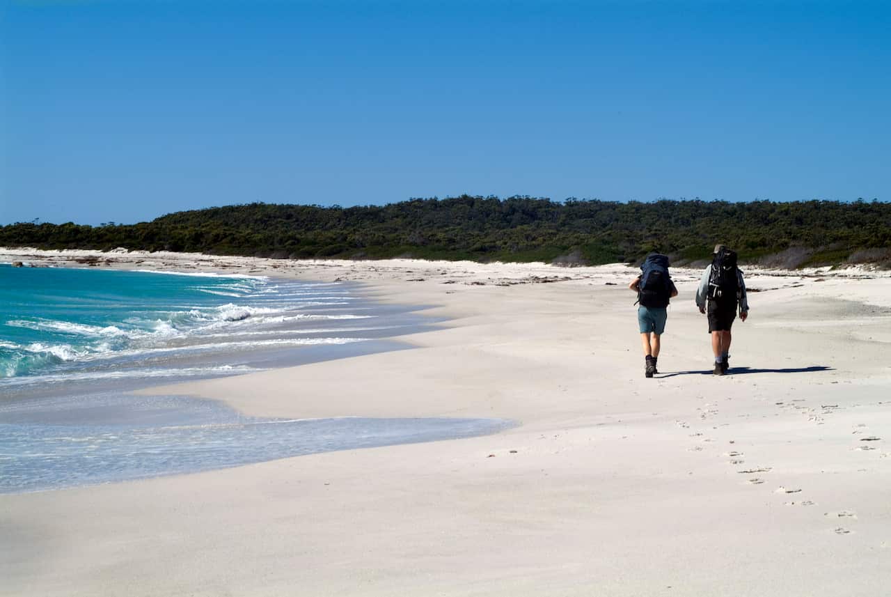 Guests of Cradle Mountain Huts walk along a remote beach on