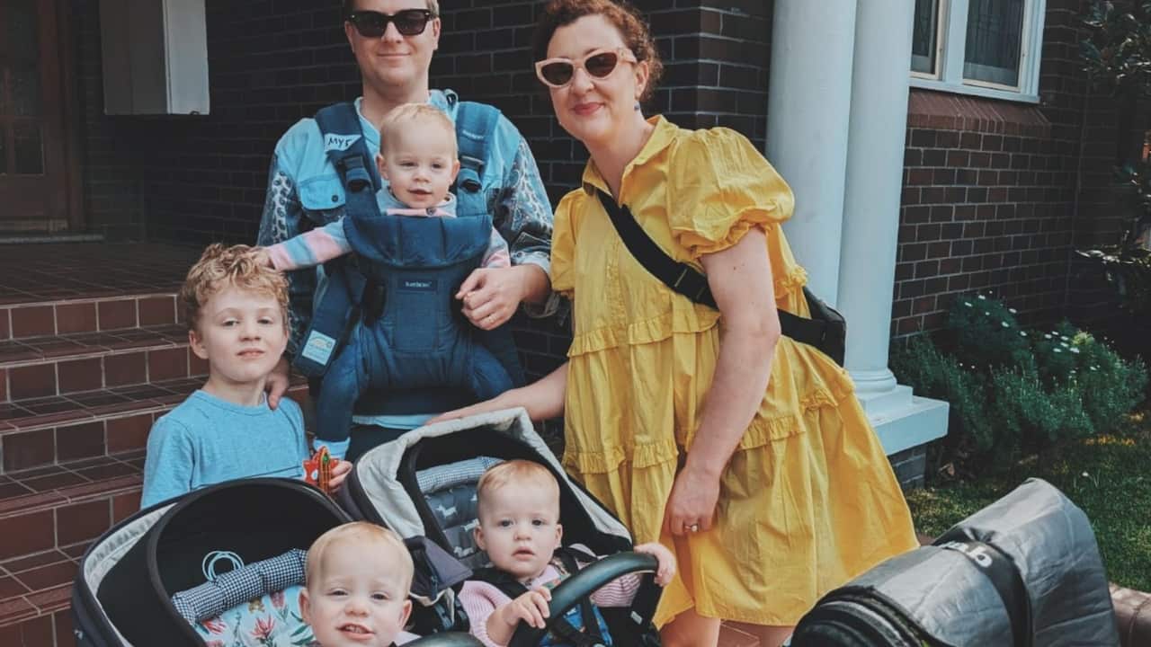 a young family of mum and dad and of three baby girls and a young boy outside a house