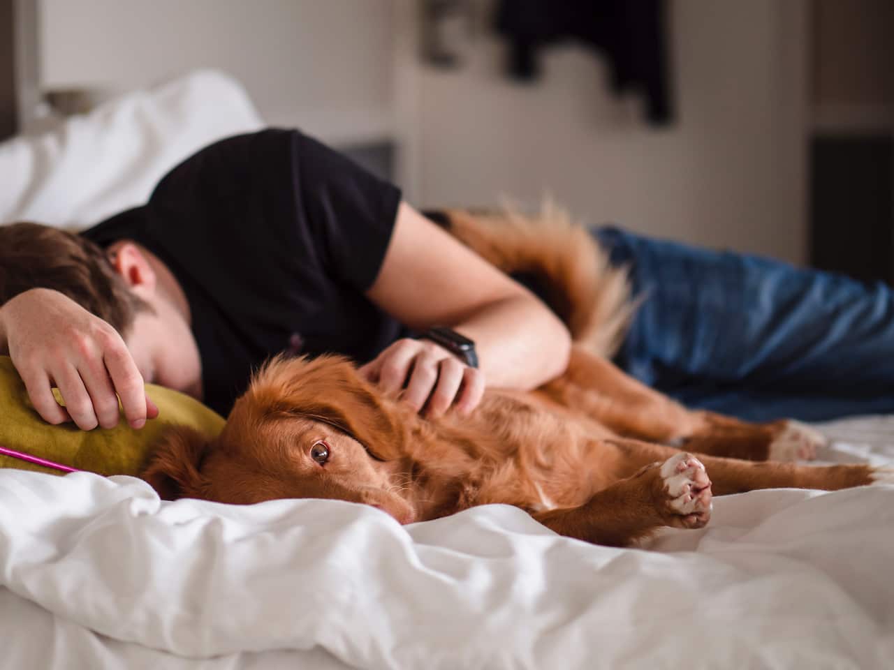 A man laying on the bed with one arm on his dog.