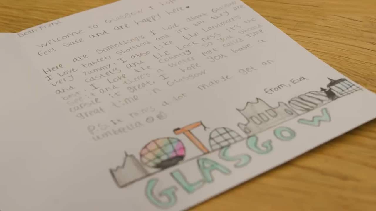 A handwritten card from a child welcoming the card's recipient to Glasgow. At the bottom of the card is a drawing of the city's skyline and bubble writing reading 'Glasgow'