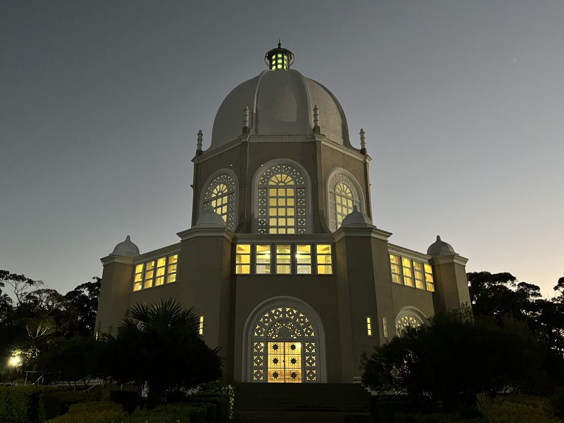 A Baha'i temple building with ornate windows at night.