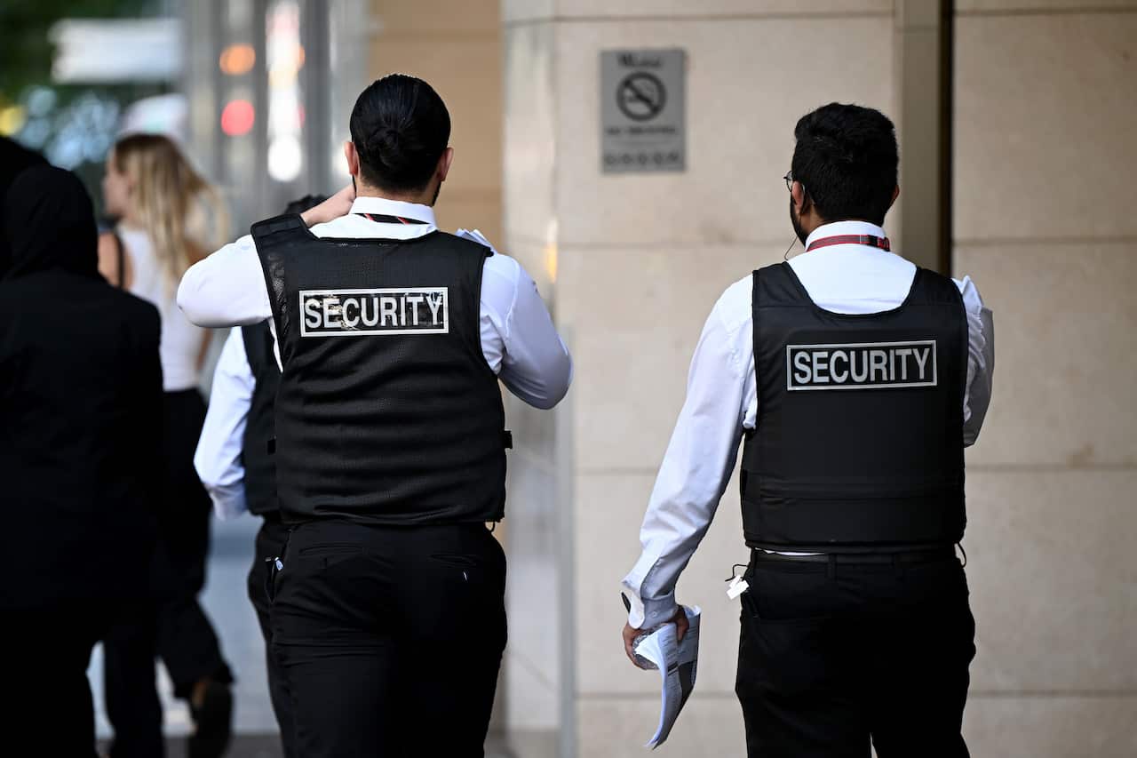 Rear view of two men wearing dark vests with Security written in capital letters across the back