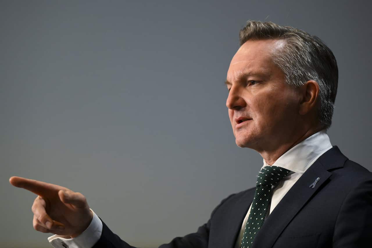 A side profile of a man in a dark suit and dotted tie, pointing his finger.