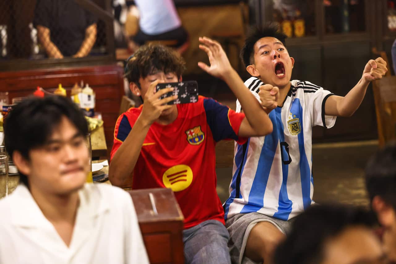 A pair of football fans, one in an Argentina shirt and the other in an FC Barcelona shirt, reacting to something that has just happened in the game.