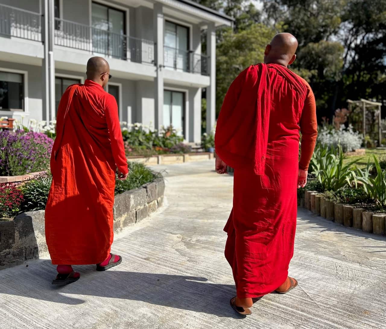 Two people wearing orange robes walk on a concrete path.