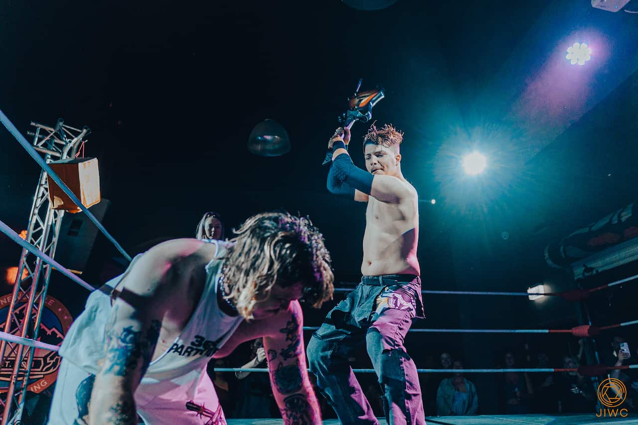 Two men in a wrestling ring. One is holding a Guitar Hero guitar.