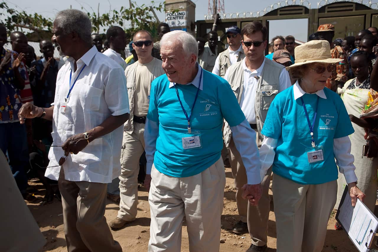 A man and a woman wearing blue shirts hold hands as they walk surrounded by a crowd.