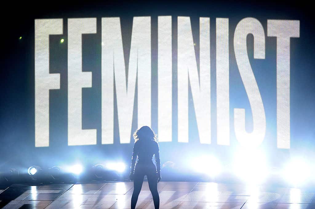A woman stands in front of lights that read Feminist.