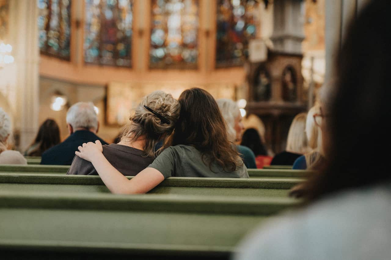 A woman sitting with arm around another on bench at protestant church