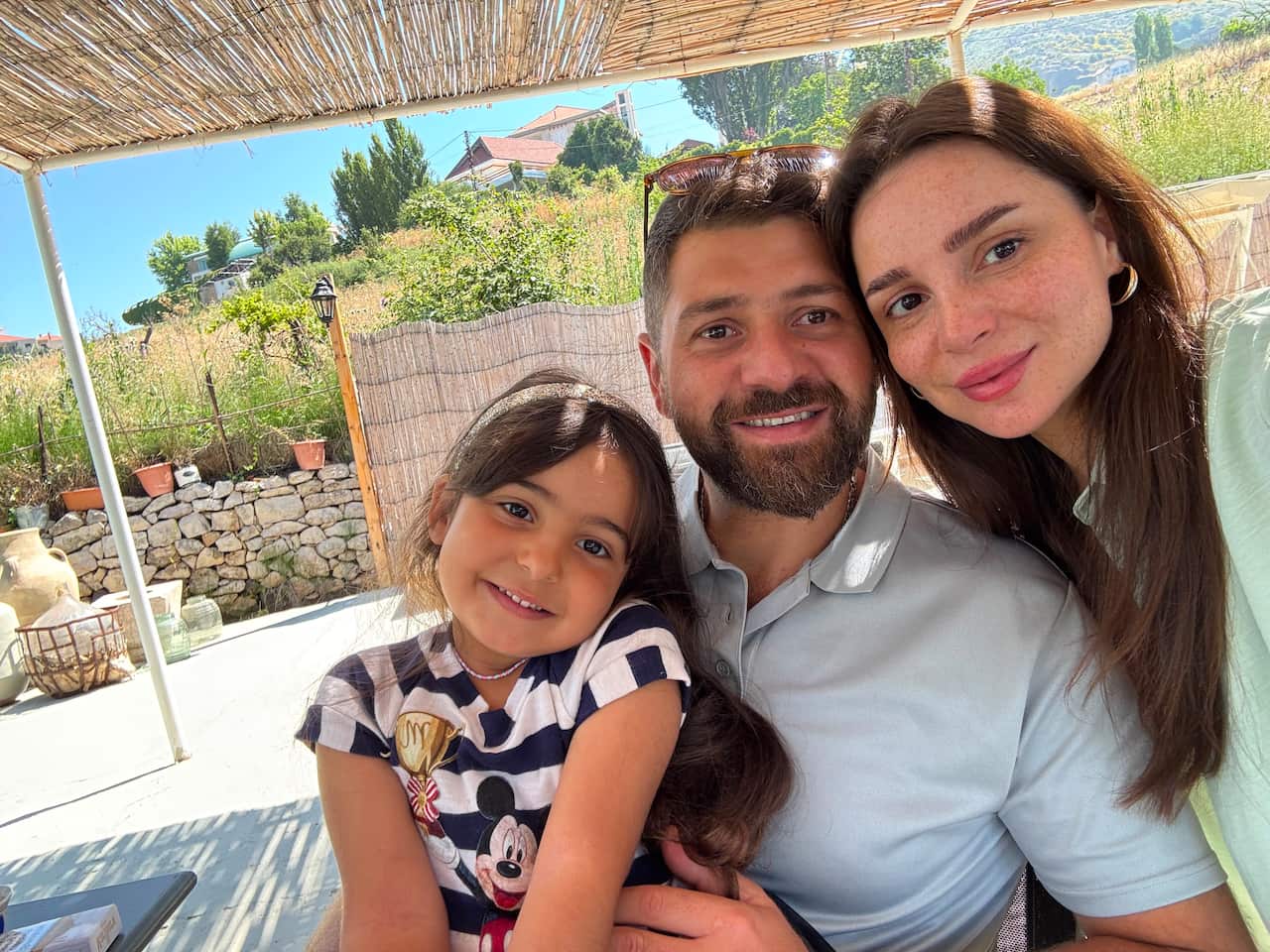 A couple posing with their young daughter under a thatched cabana.