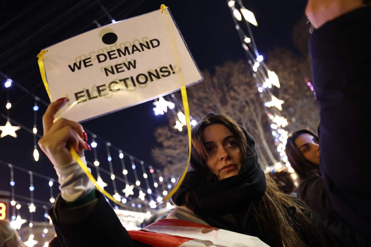 A woman holding a sign with 'We Demand New Elections' written on it.