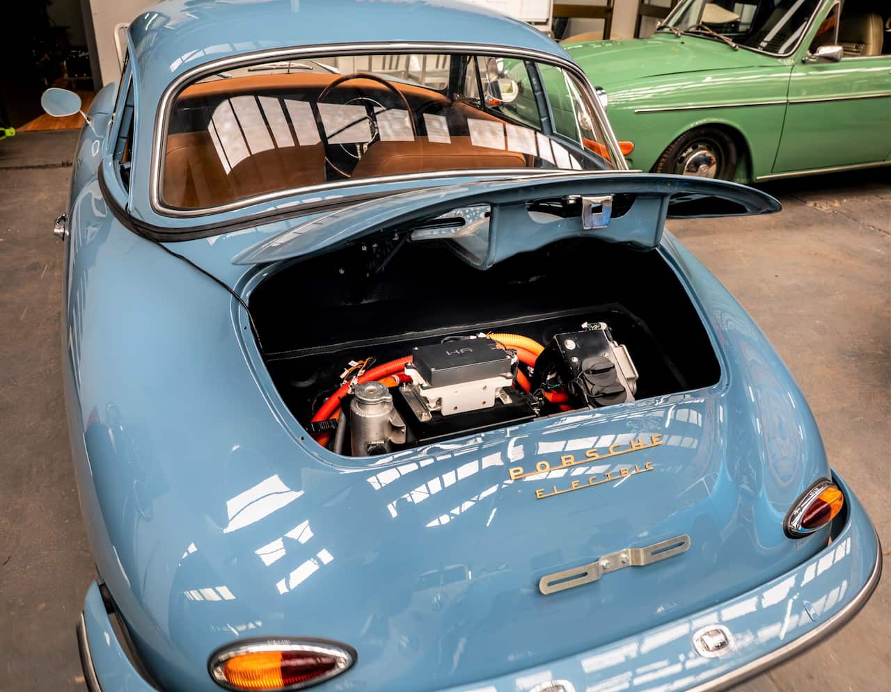 A shiny blue vintage car has the boot open to reveal an electric battery.