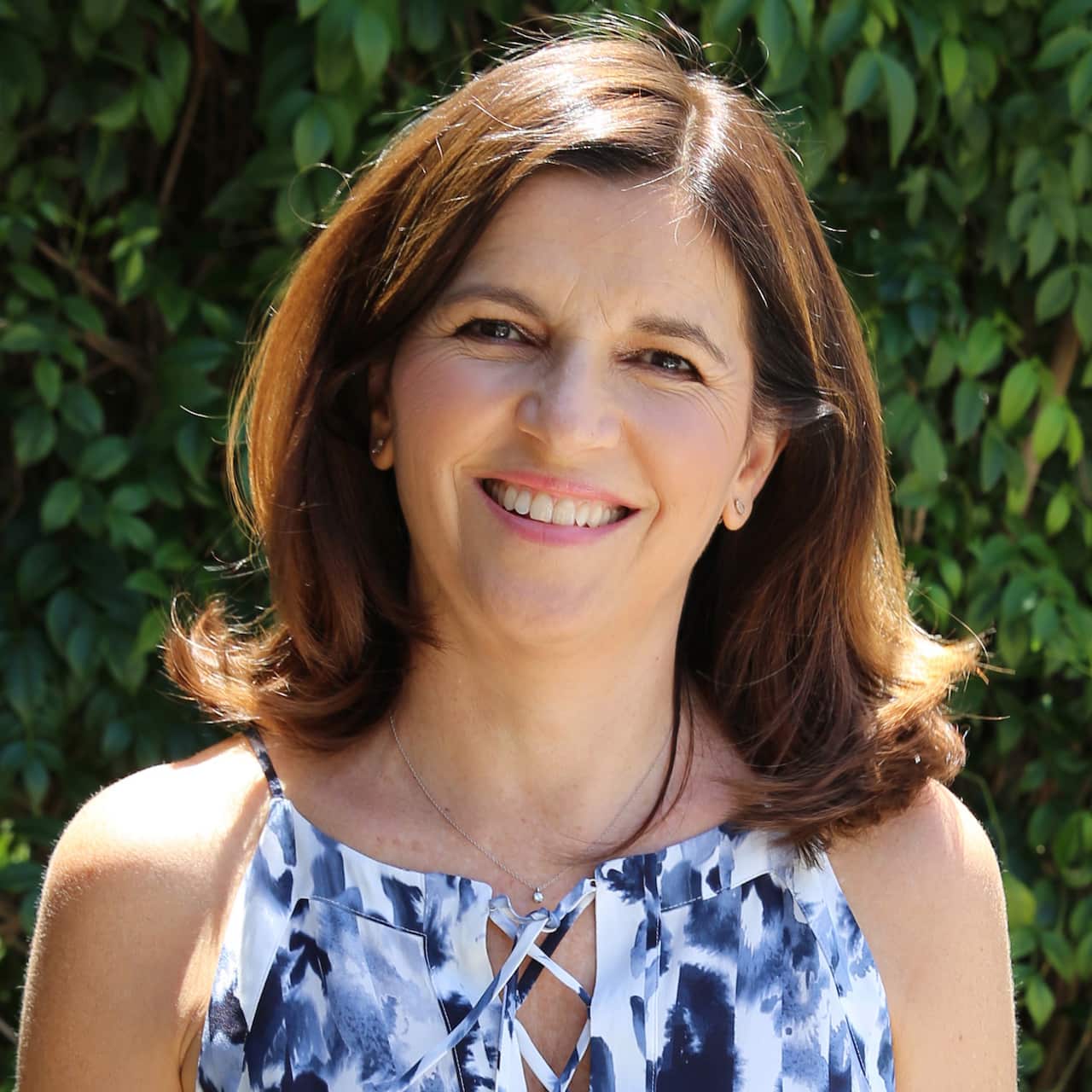 A smiling woman in front of greenery.