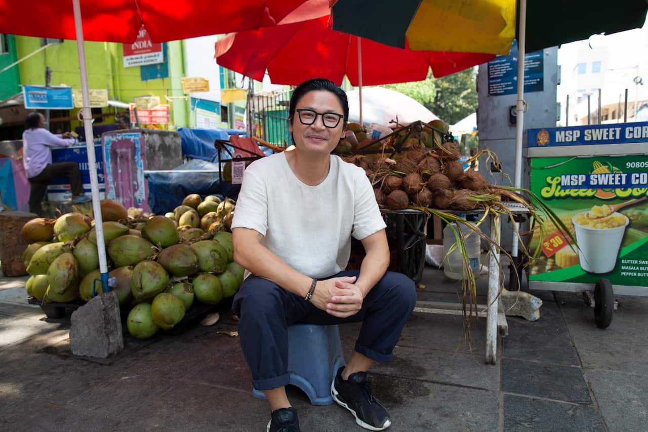 Luke Nguyen sits in front of a food stall in India