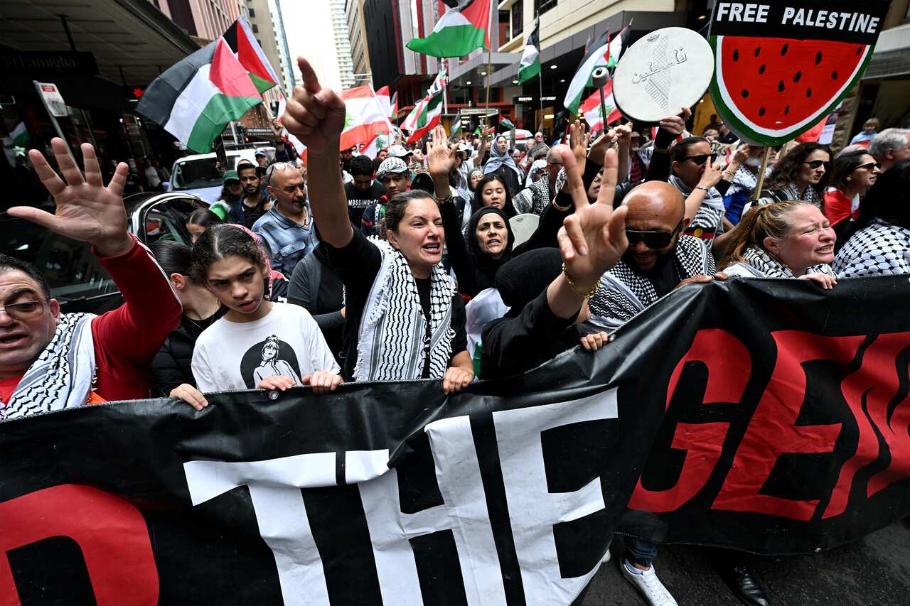 People at a protest holding a banner. Some are waving Palestinian flags and holding signs that say Free Palestine.
