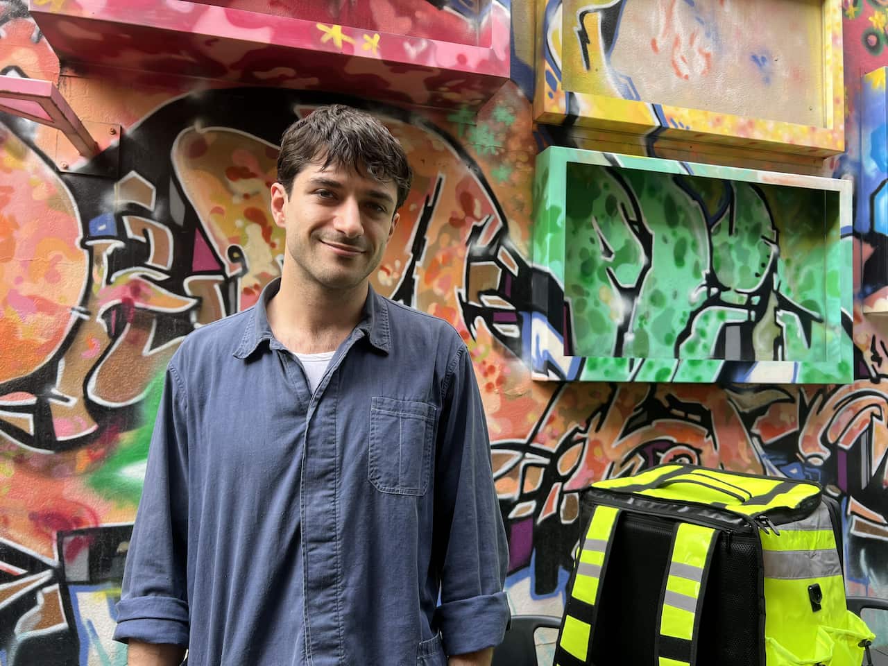 A man stands in front of a wall of graffiti.