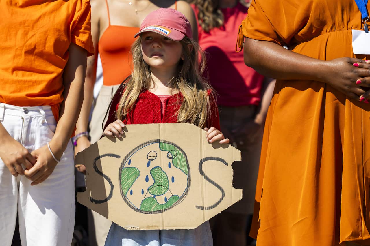 A young girl holding a piece of cardboard with "SOS" written on it. The O is a globe that is crying.