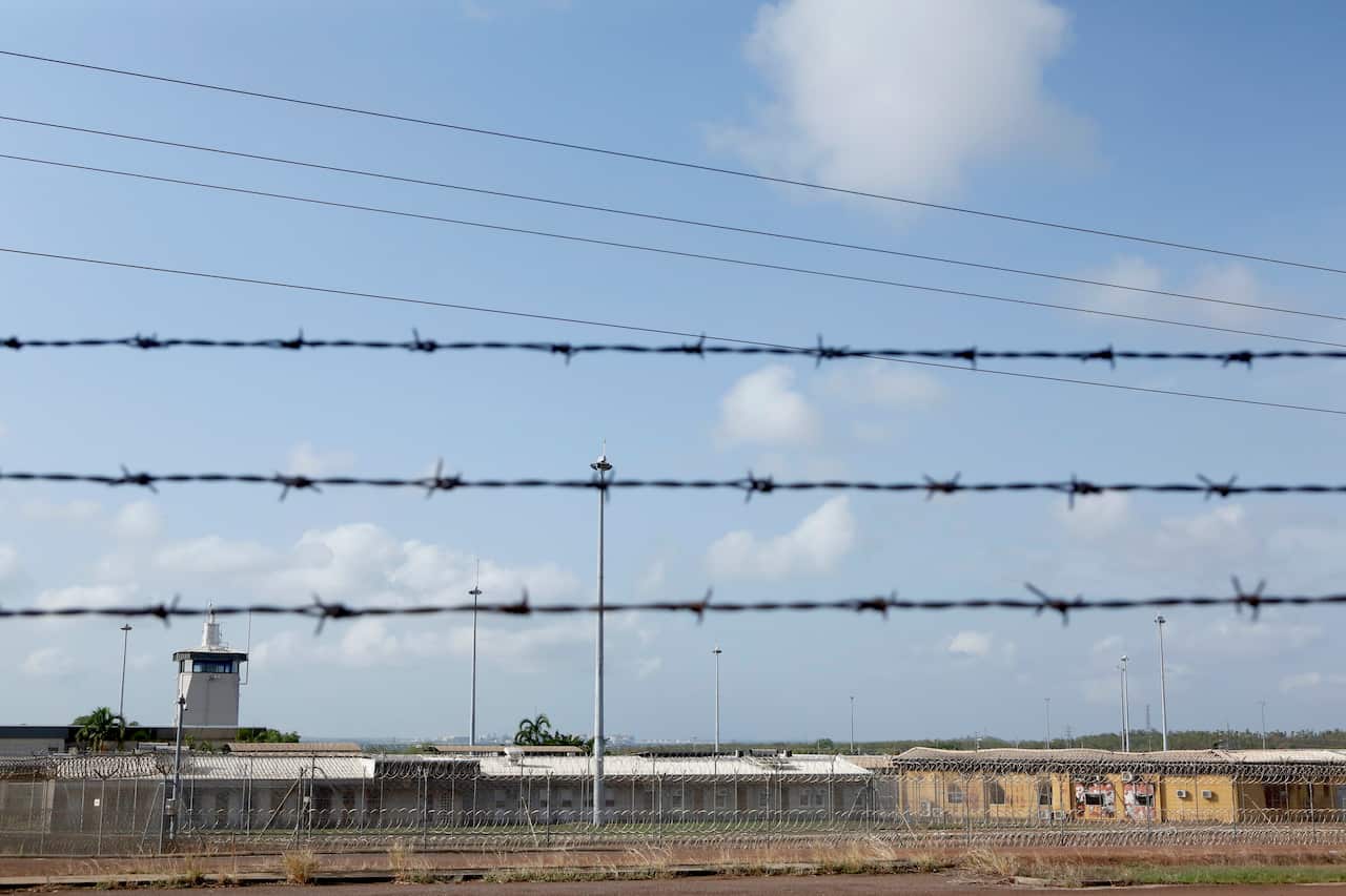 Buildings that make up the Don Dale Detention Centre in the background, with lines of barbed wire in the foreground.