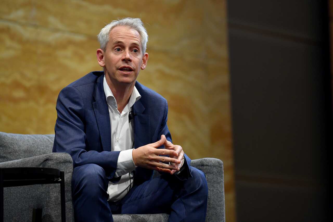 Man in dark blue suit sitting in a chair and talking.