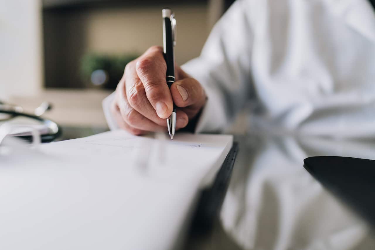 Close-up of a doctor's hand as he writes on a notepad.
