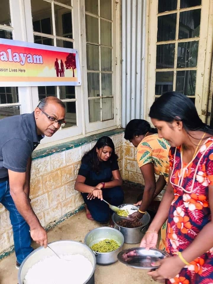 A man and women serve food from large pots into dishes for two women.