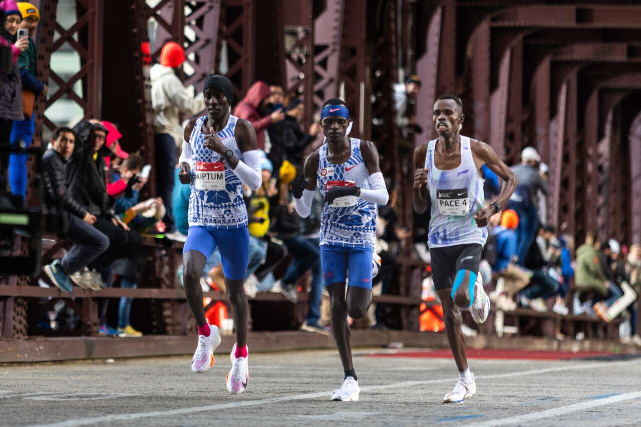 Three men running a marathon as people watch on.