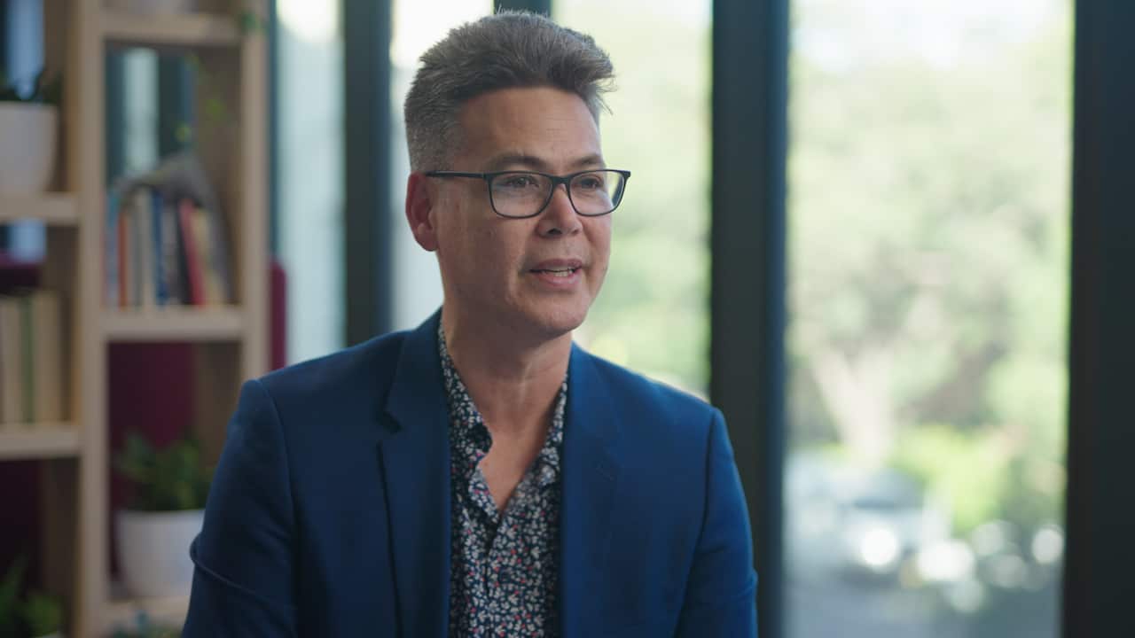 A man with glasses in a blue suit smiles at the camera