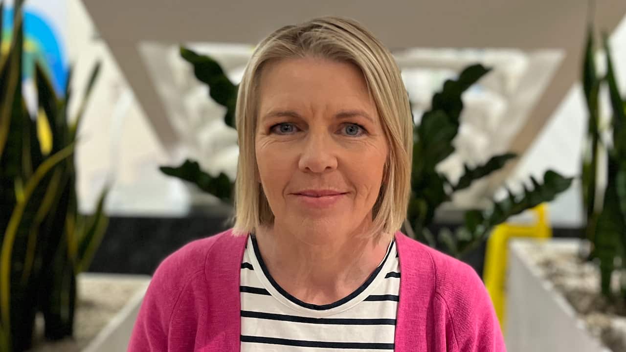 a closeup shot of a middle aged blonde woman wearing a pink cardigan