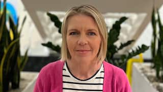 a closeup shot of a middle aged blonde woman wearing a pink cardigan
