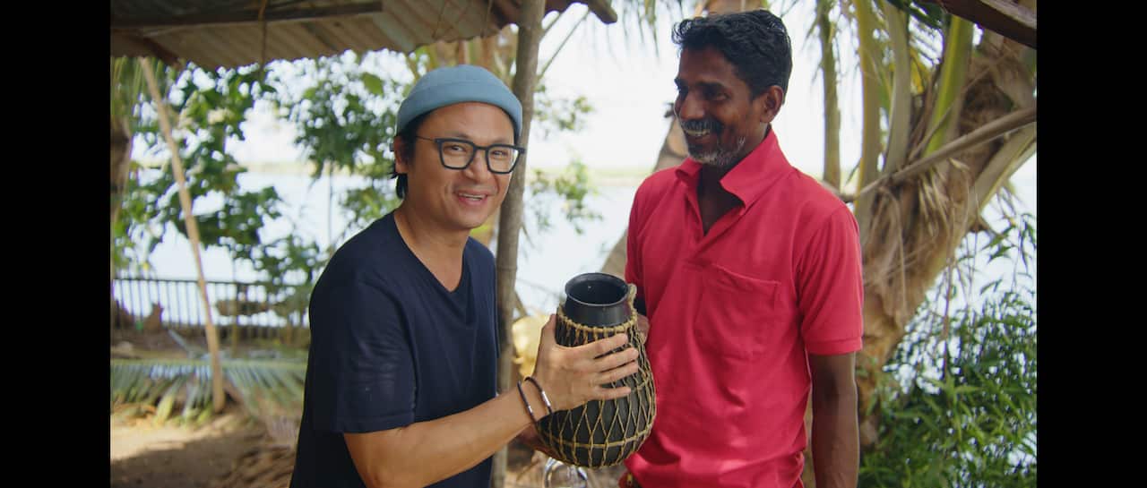 Luke Nguyen (left) holding a jug and smiling with a man and trees in the background.