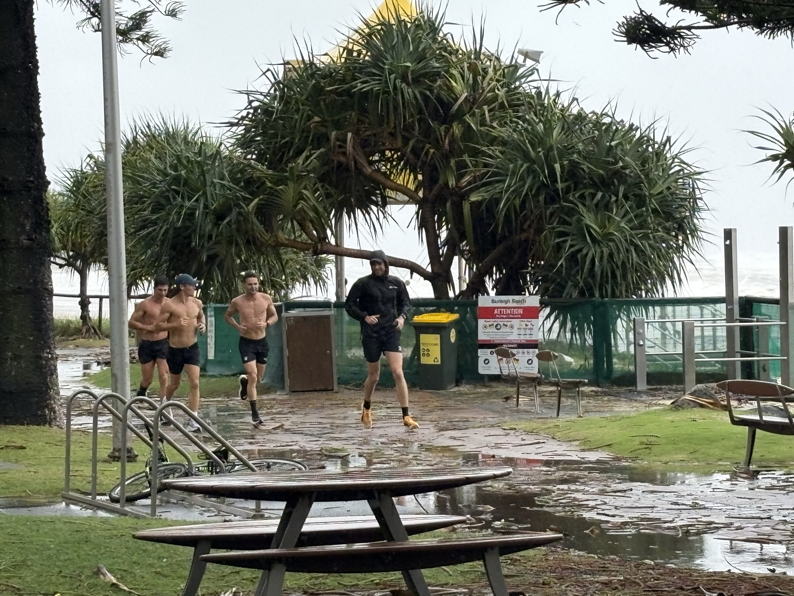 A group of four runners run along a muddy track in a park. The ocean is in the background
