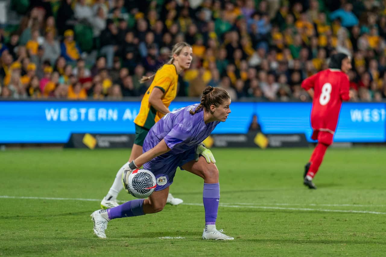 Teagan Micah passing a football on a green pitch. There is another Matilda behind her, and audience members in the seats.