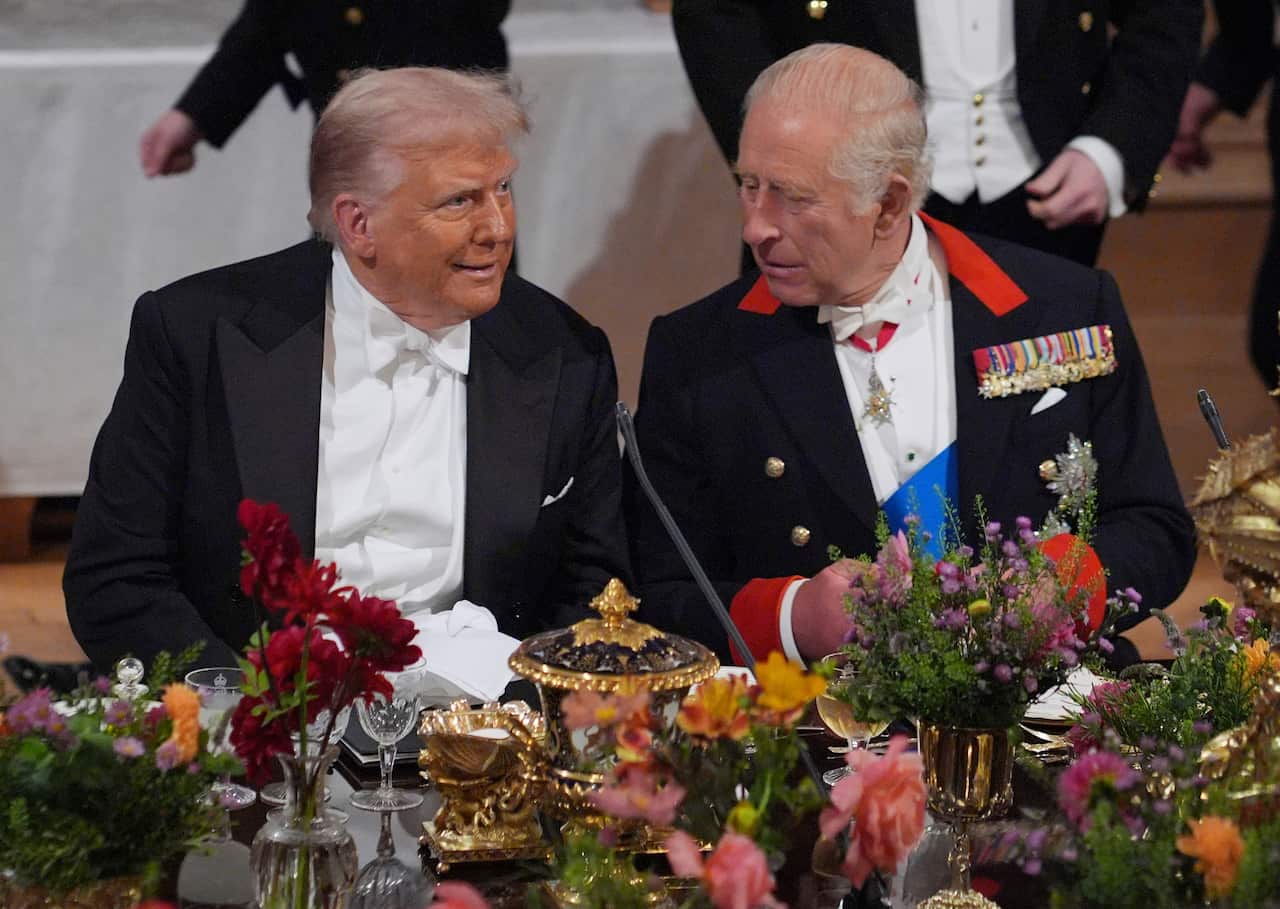 Donald Trump and King Charles seated at an elegant table, talking to each other.