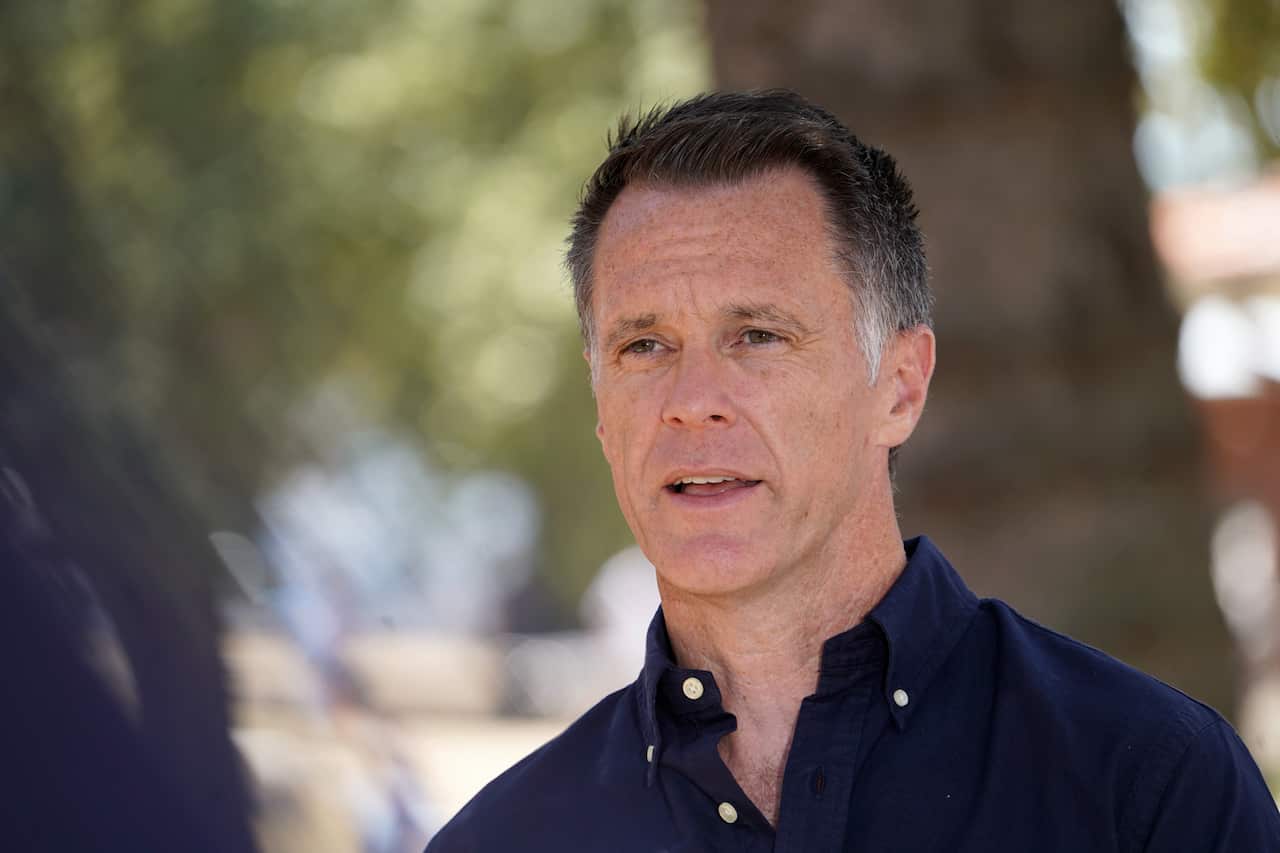 A man wearing a dark blue shirt standing in front of a tree.