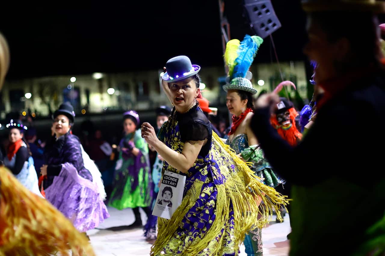 Women dancing in the street in Chile. They are wearing long colourful skirts and black bowler-style hats