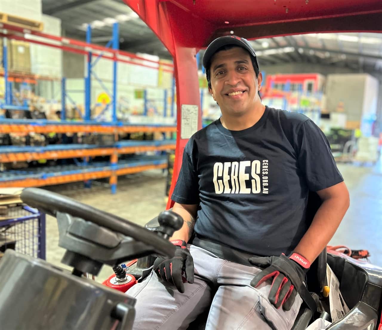 A man in a cap and black t-shirt sitting in a forklift. 