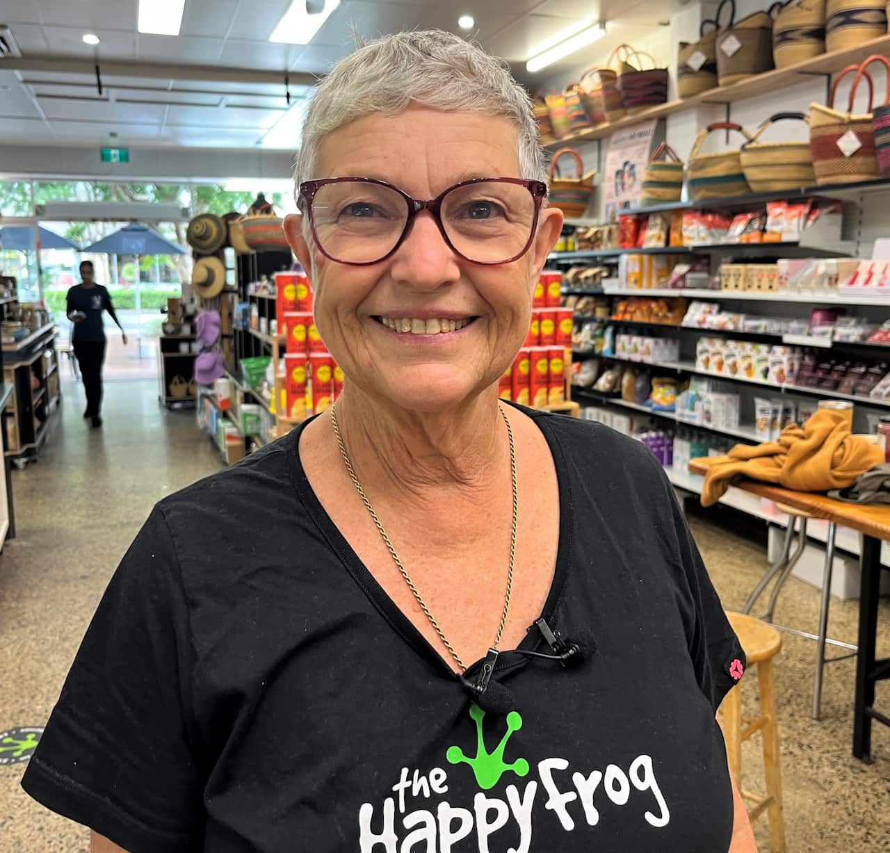 A woman in a black t-shirt stands in a cafe smiling at the camera.