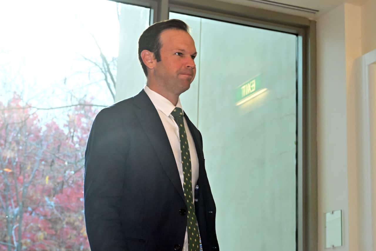 A man wearing a suit and tie stands in front of a glass door.