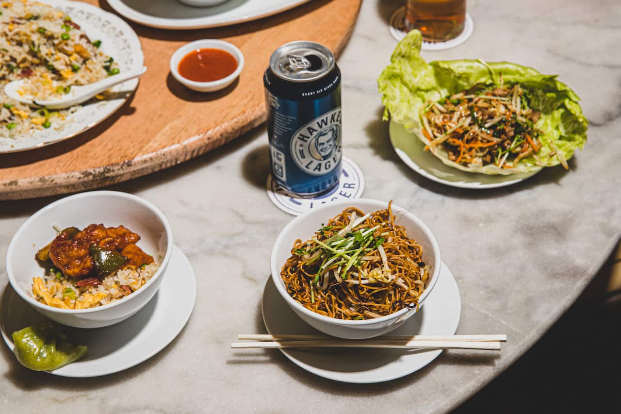 Bowls and plates of Chinese food sit on a table next to a Lazy Susan