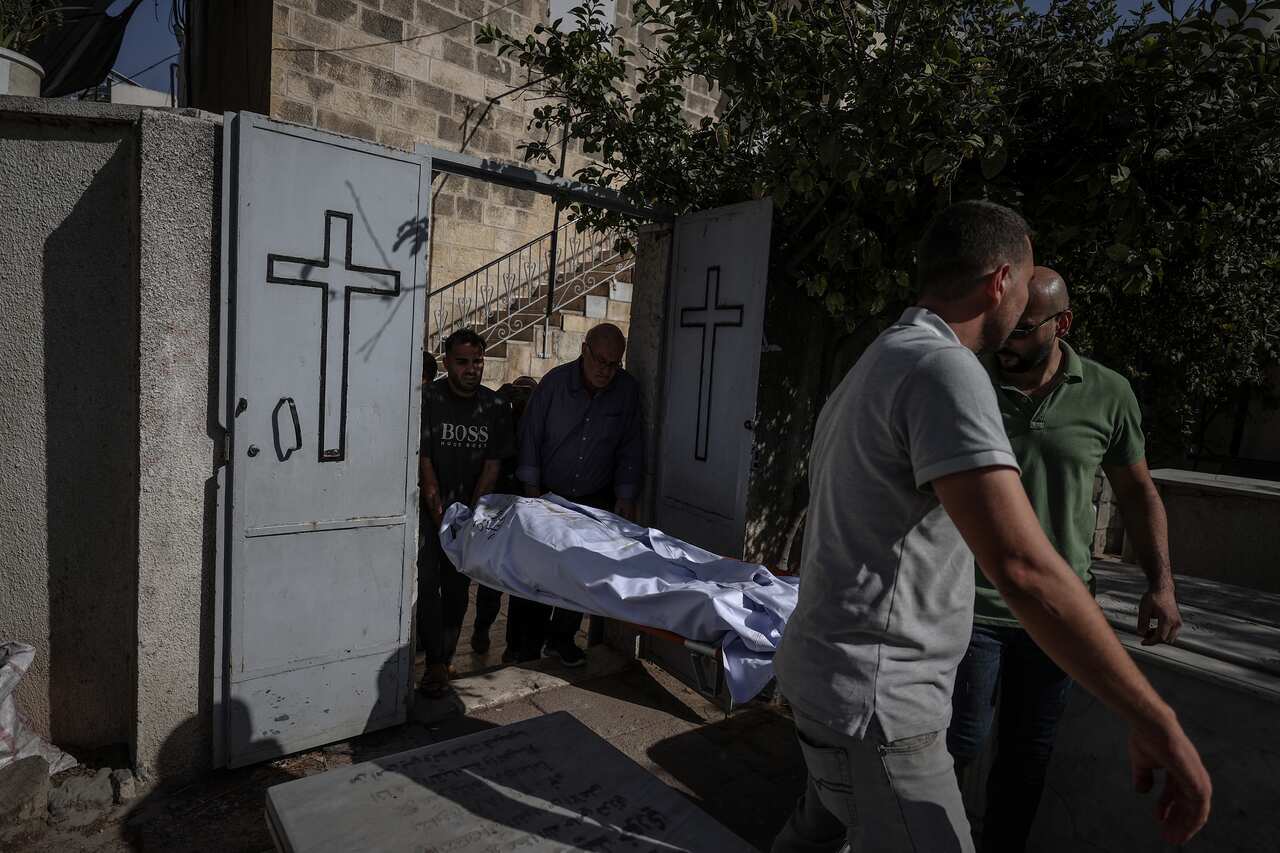 Four men carry a body bag on a stretcher through gates with cross symbols.