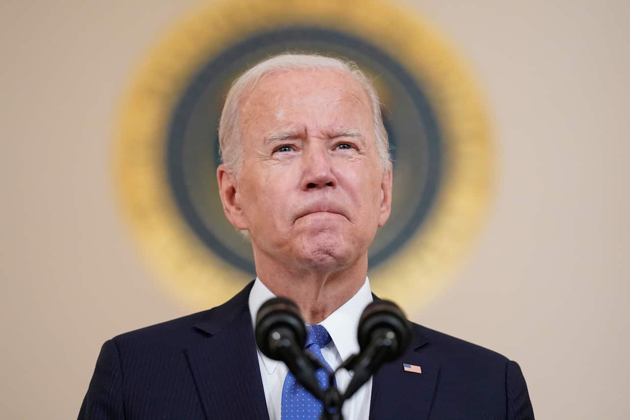 US President Joe Biden purses his lips as he stands in front of a microphone. 