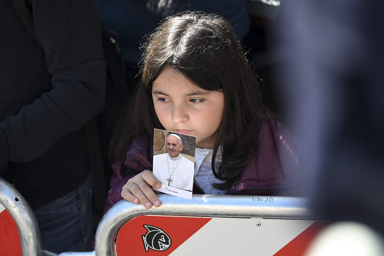 A young girl standing behind a barricade holds up a photo of Pope Francis.