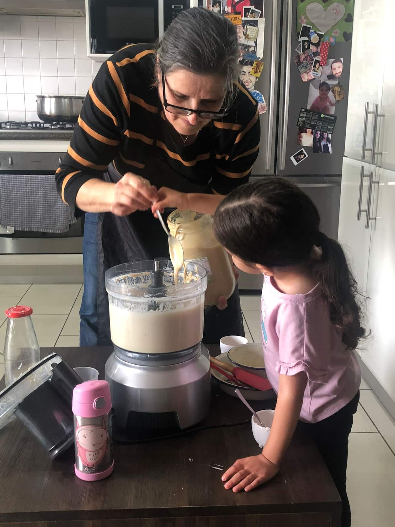 A woman makes hummus with a young girl.