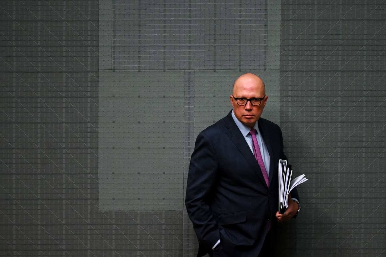 Man in glasses holding documents standing in front of a wall.