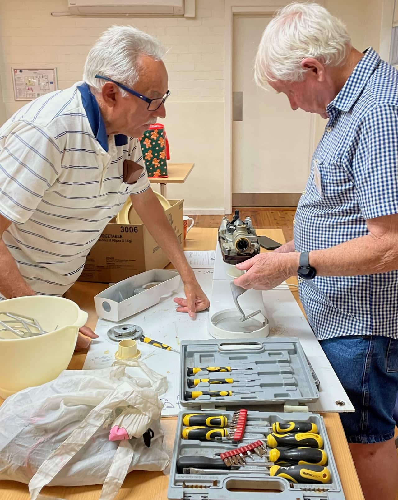 Two men stand at a table covered with electronic equipment. 